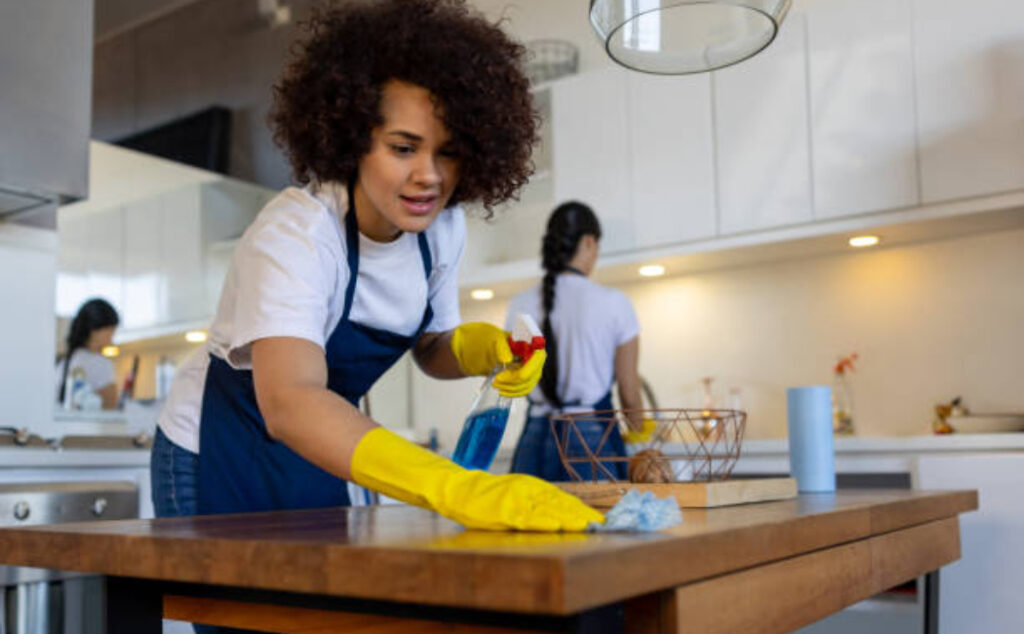 A cleaning expert is using a cloth to clean the dining table in the kitchen