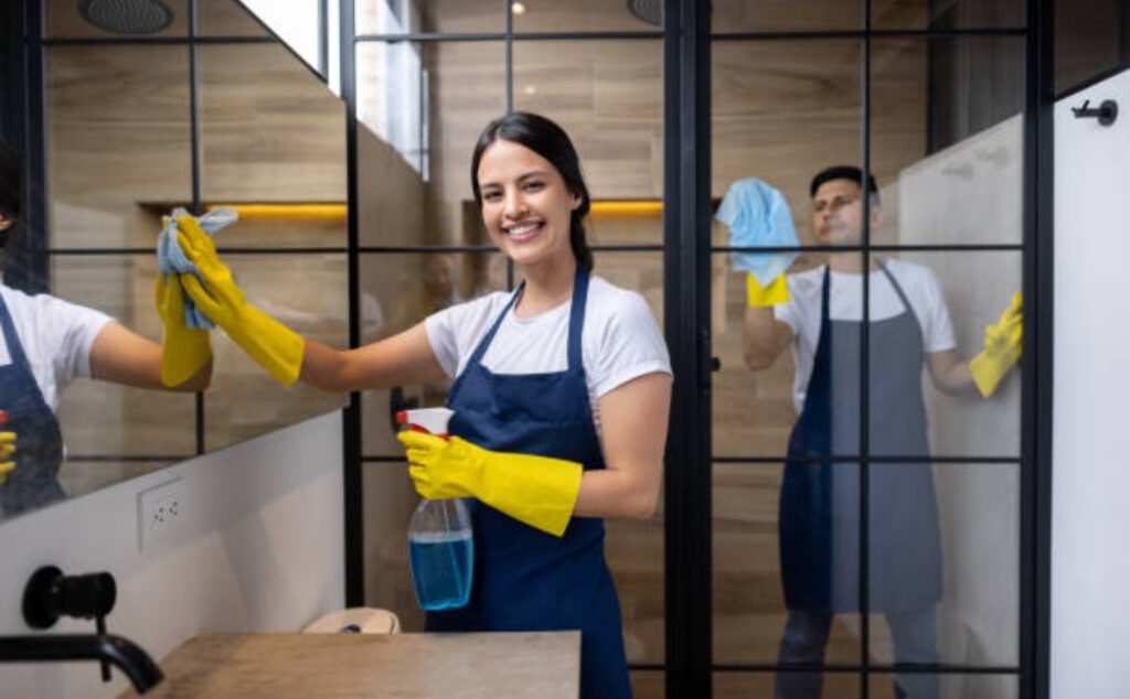 Two smiling professional cleaners are cleaning a modern bathroom.