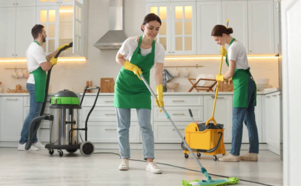 A team of janitors in protective uniforms is cleaning a commercial kitchen