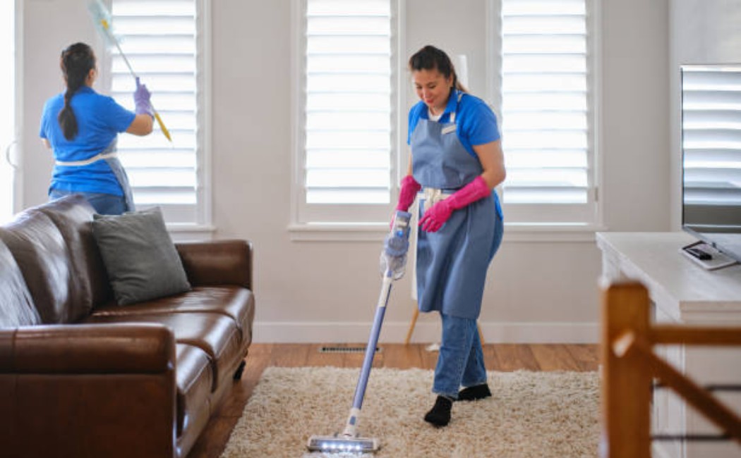 Two professional cleaners wearing gloves, dusting and wiping surfaces in a modern home.