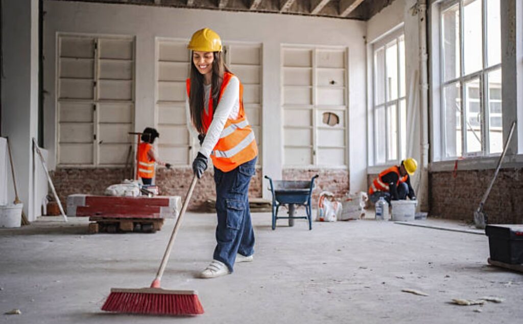Female construction worker sweeping floor at a job site