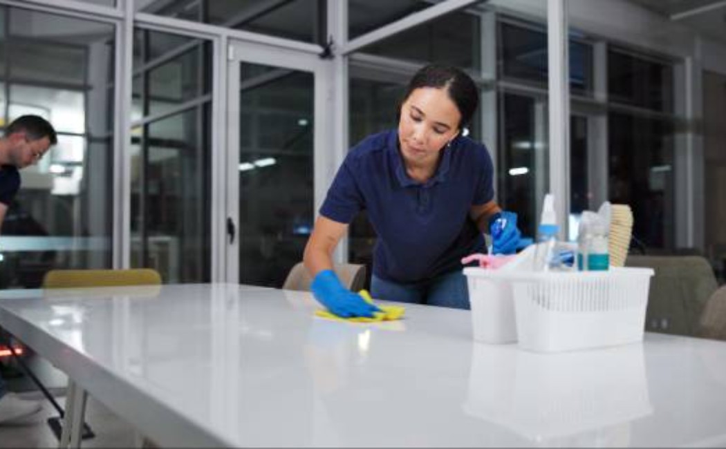 Cleaner wearing safety gear sanitizing office furniture.