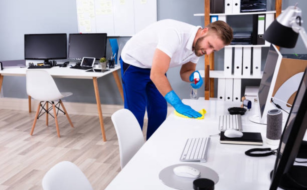 Janitor cleaning a white office desk with cleaning supplies